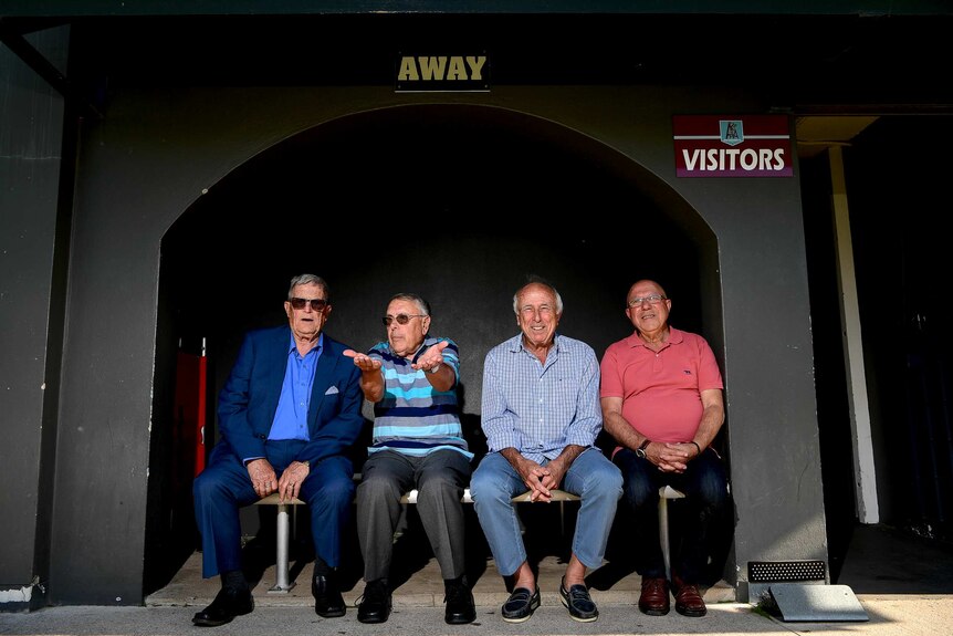 Four old men sit on a bench under the 'visitors' and 'away' signs.
