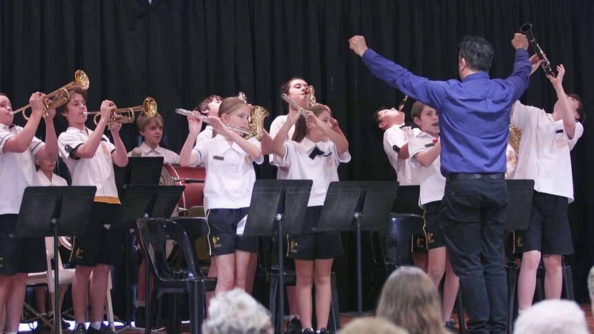 A primary school band standing up and playing out! The conductor has raised his fists.