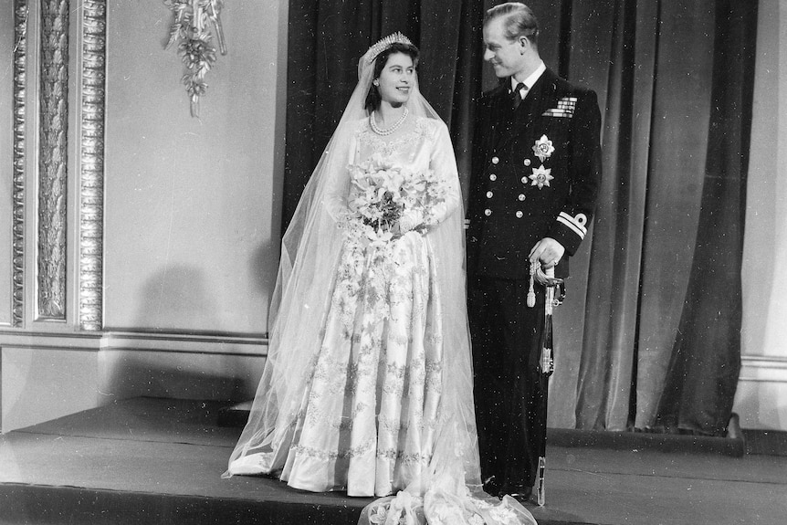 Queen Elizabeth and Prince Philip stand in their wedding outfits.