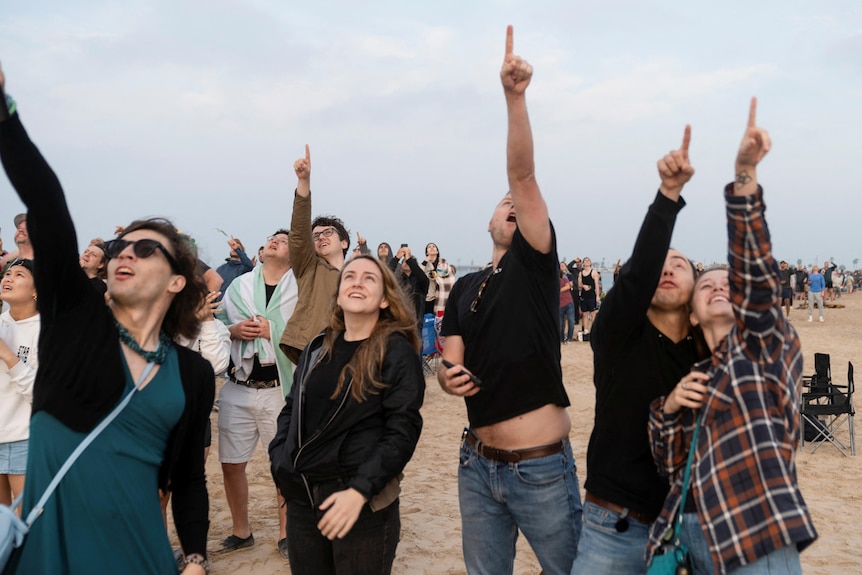 Spectators gather to watch the spacecraft launch in Texas. They all point at the sky