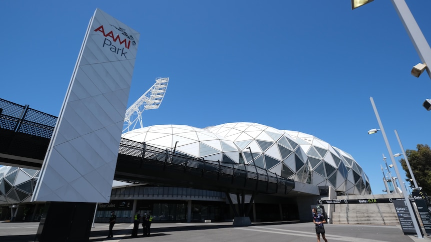 A lone man stands in front of a modern-looking building with white, diamond-shaped domes.