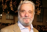 Stephen Sondheim smiles towards the camera wearing a brown suit jacket