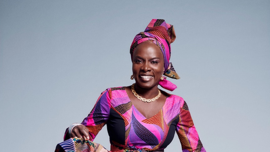 A woman in African headress and bright sparkly tights dances, smiling in a colourful dress.