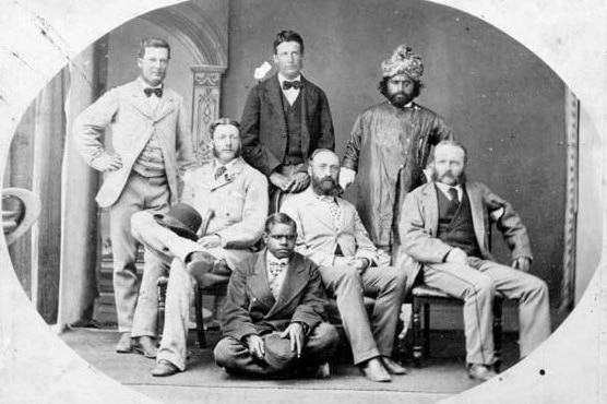 A black and white photograph from 1875 featuring seven men, some standing, some sitting including an Aboriginal youth