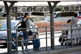 A woman pulling a suitcase outside an airport wears a face mask.