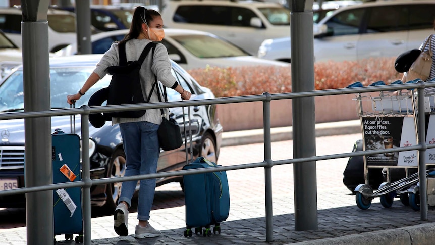 A woman pulling a suitcase outside an airport wears a face mask.