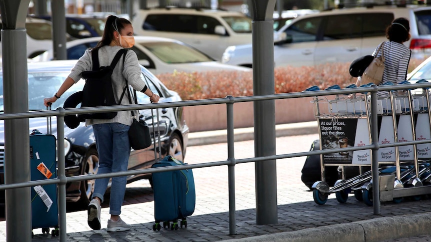 A woman pulling a suitcase outside an airport wears a face mask.