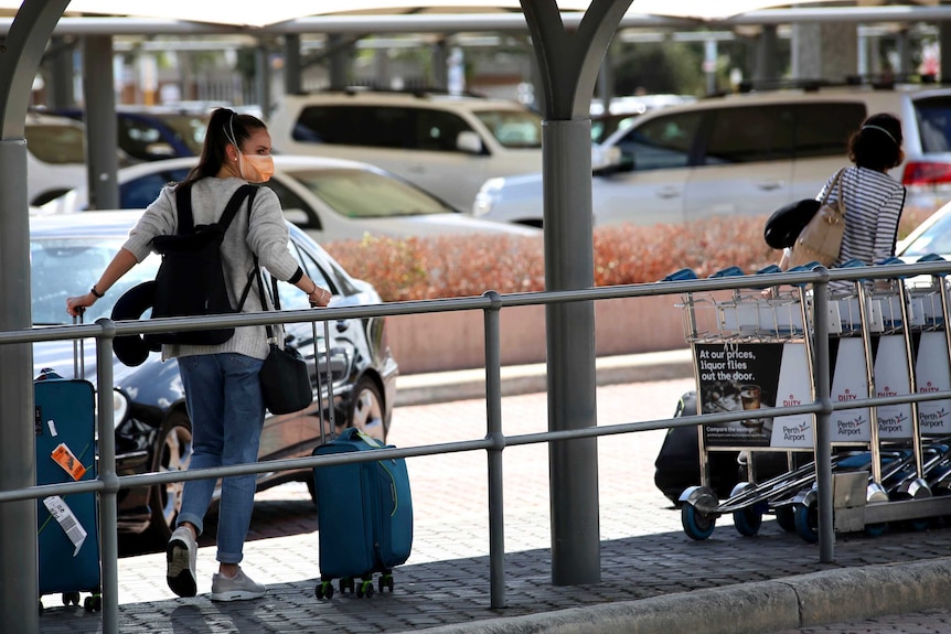 A woman pulling a suitcase outside an airport wears a face mask.