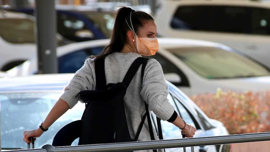 A woman pulling a suitcase outside an airport wears a face mask.