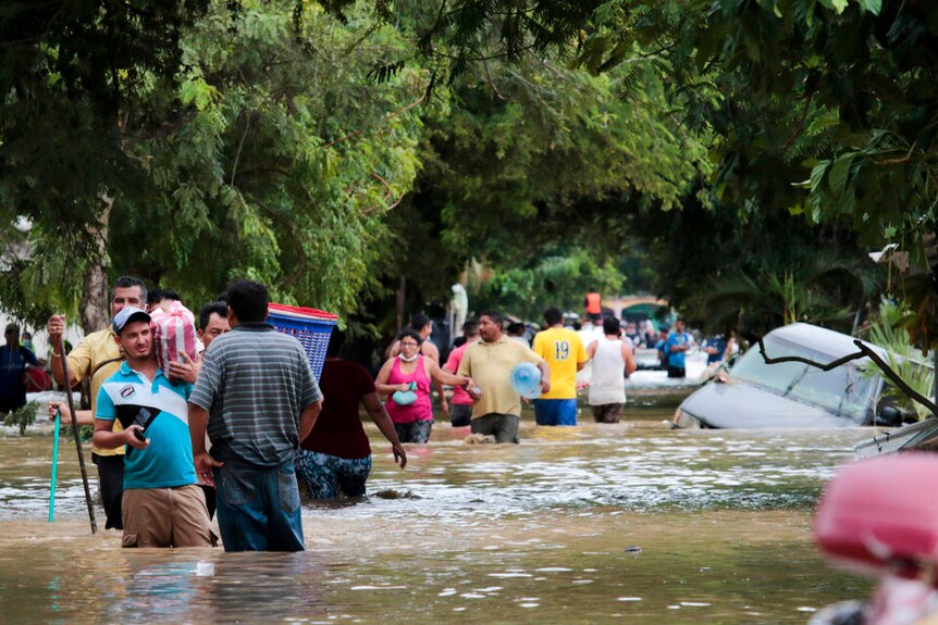 Residents walk past inundated vehicles in the flooded streets of Planeta, Honduras.