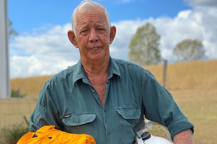 Man in a green shirt holding his rural fire helmet and yellow rural fire jacket