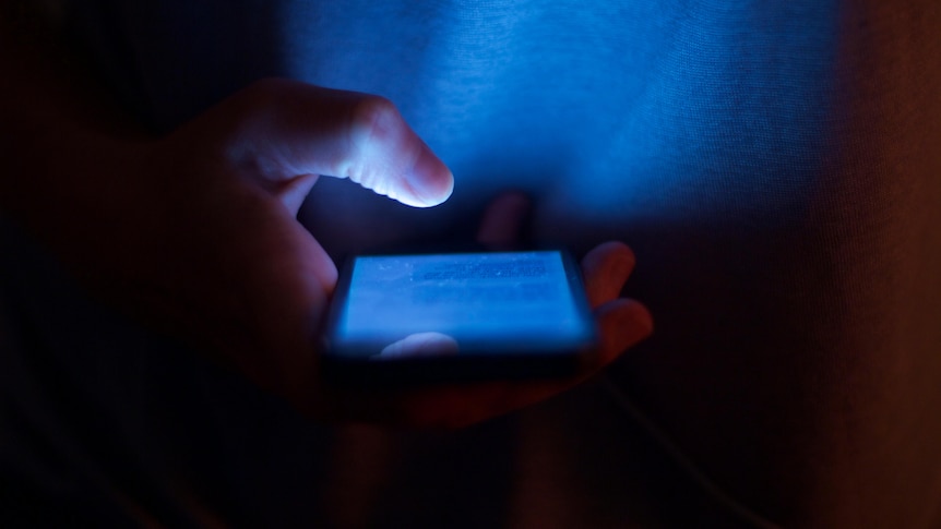 Image of a person typing on their phone, reading messages. It's dark and only the phone is creating light.