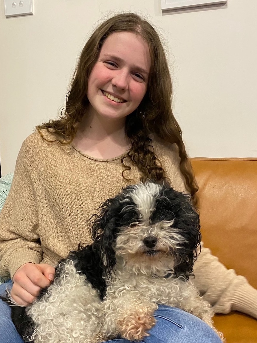 A girl with long hair sits on a couch with a dog