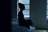 The silhouette of a woman sitting on end of bed. 