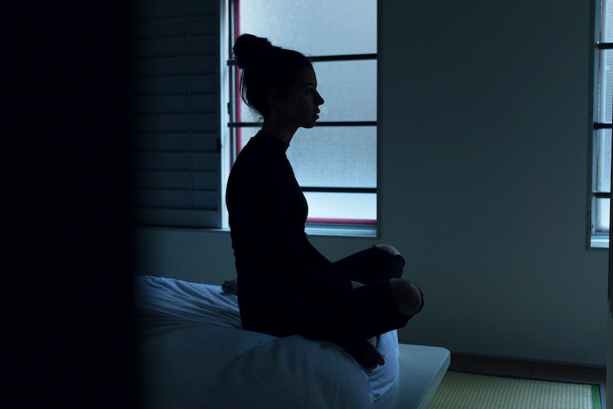 The silhouette of a woman sitting on the end of the bed. 