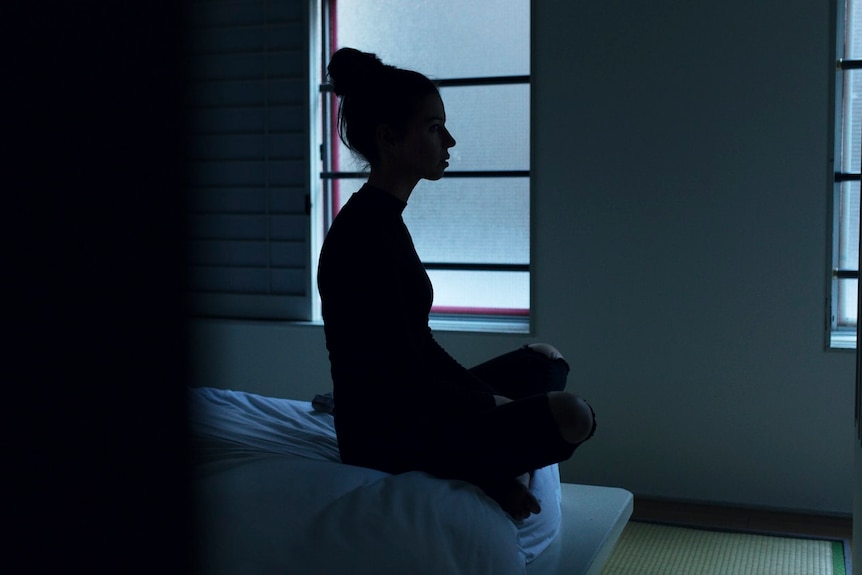 The silhouette of a woman sitting on end of bed. 