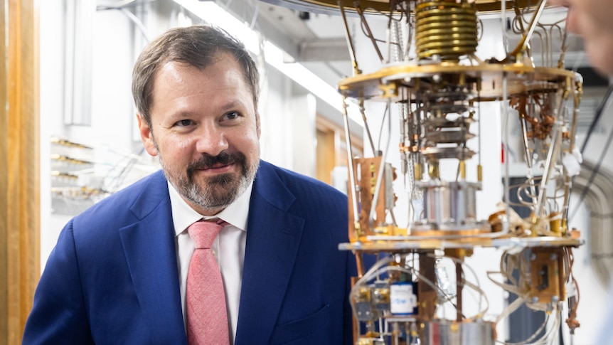 A man in a suit looks at a wired technological contraption.