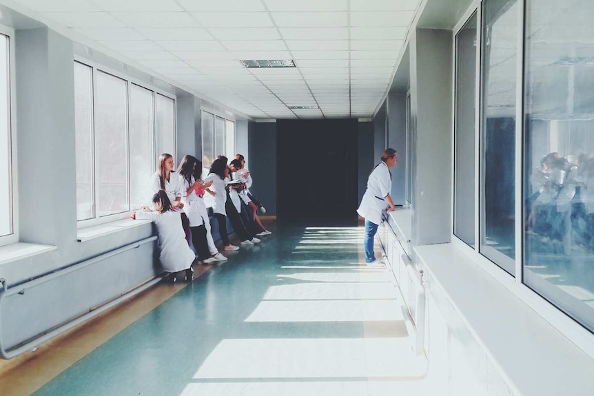 A doctor and group of medical students look through window to hospital room