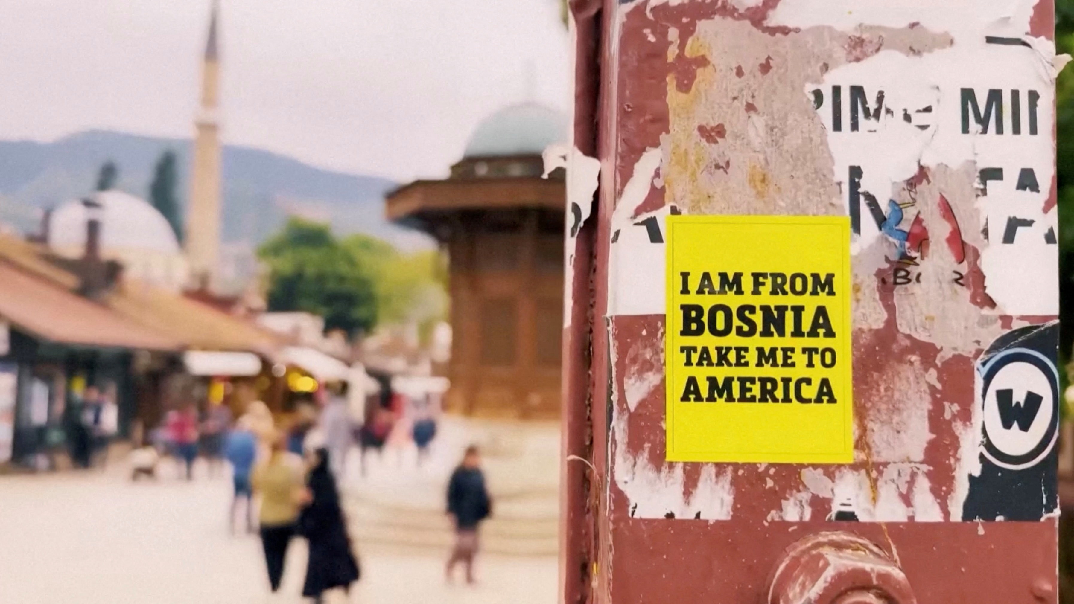 A sticker that reads I am from Bosnia take me to America, stuck on a pole
