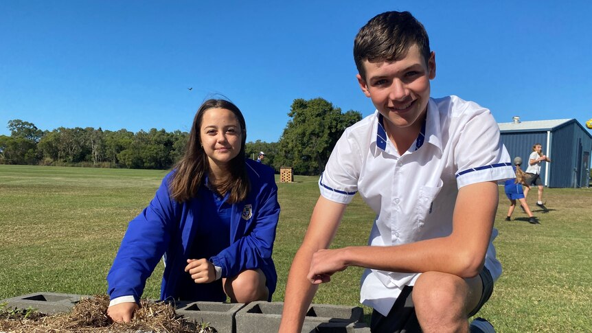 Mackay North State High School students Tamlyn Nell and Aaron Bickford kneel next to a soil patch, each resting a hand on it