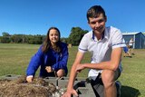 Mackay North State High School students Tamlyn Nell and Aaron Bickford kneel next to a soil patch, each resting a hand on it