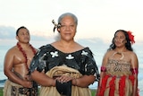 Fiame Naomi Mata'afa stands in front of a man and woman, all in traditional Samoan garments, on a beach at dusk.