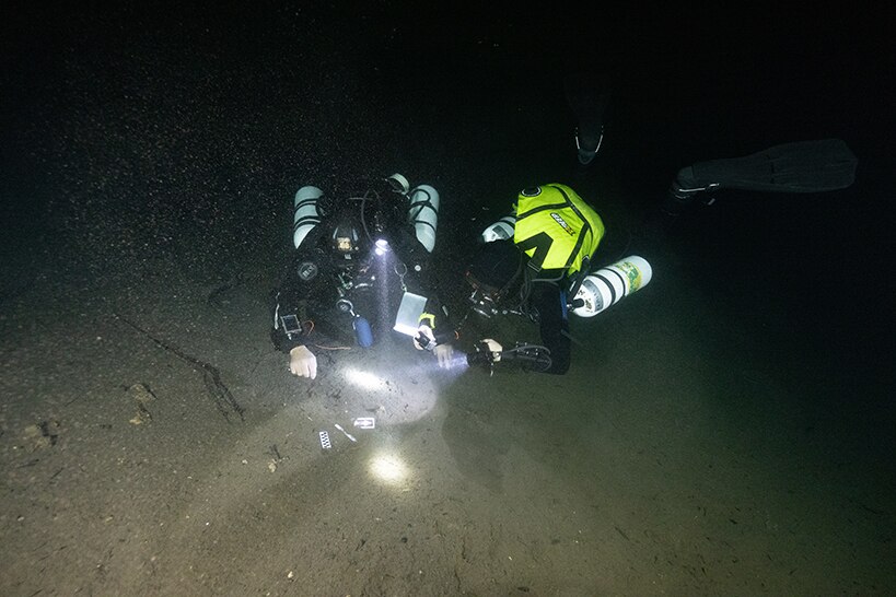 Two divers use torches to search the sea bed