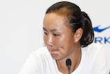 Peng Shuai looks to the side while sitting at a desk for a press conference with a microphone in front of her.