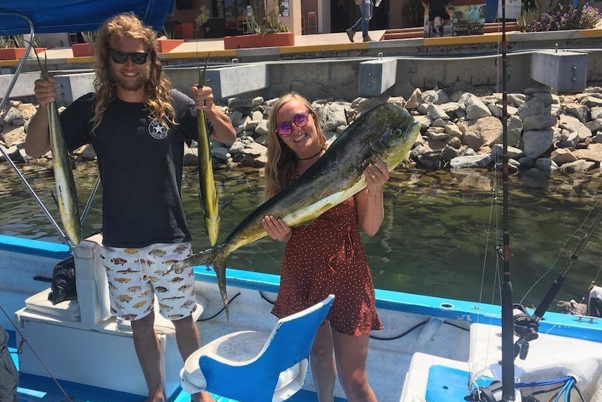 Two young people on a boat with caught fish.