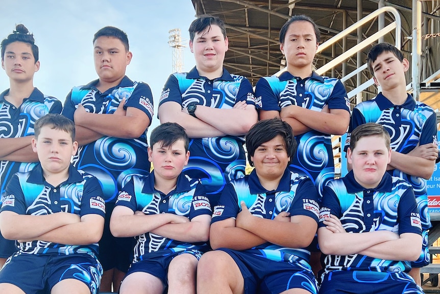 A team photo of young boys crossing their arms and looking serious while wearing blue netball uniforms