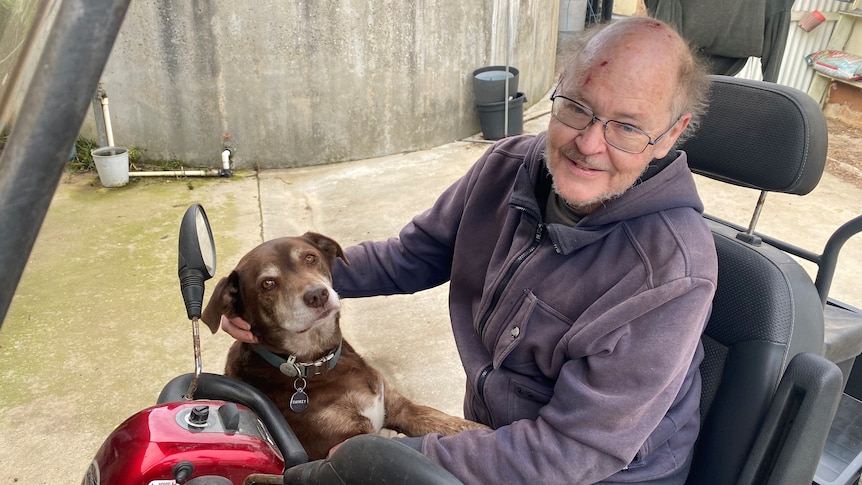 Man sitting on red gopher in black seat with red kelpie sitting with paws on his lap, both looking at camera