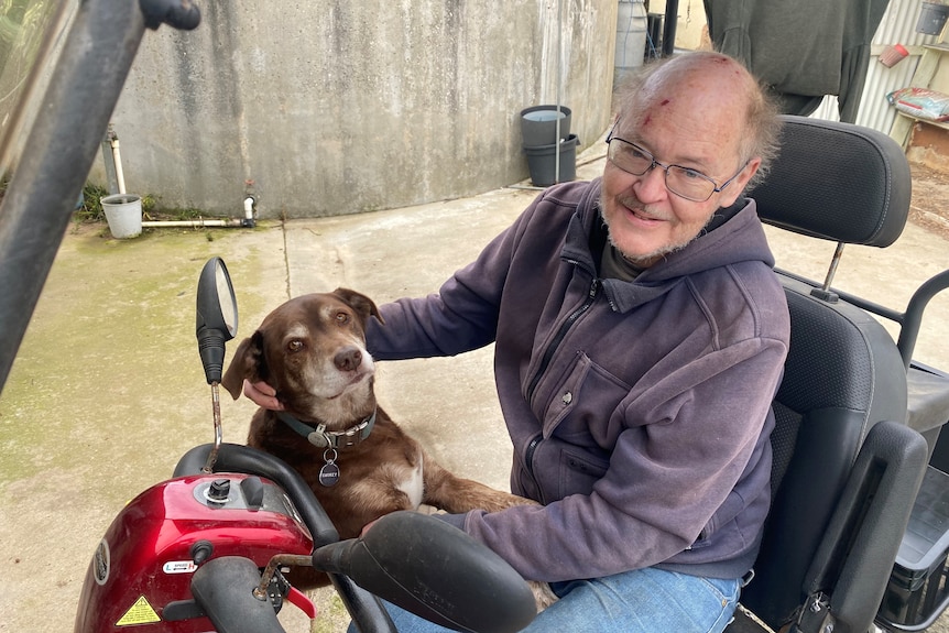 Man sitting on red gopher in black seat with red kelpie sitting with paws on his lap, both looking at camera