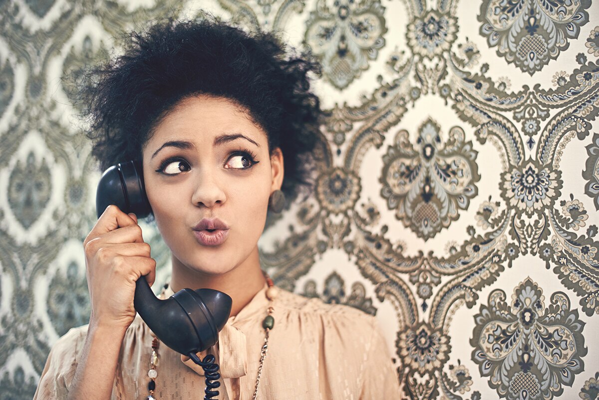 A women in 70s clothing holds an old style landline telephone.