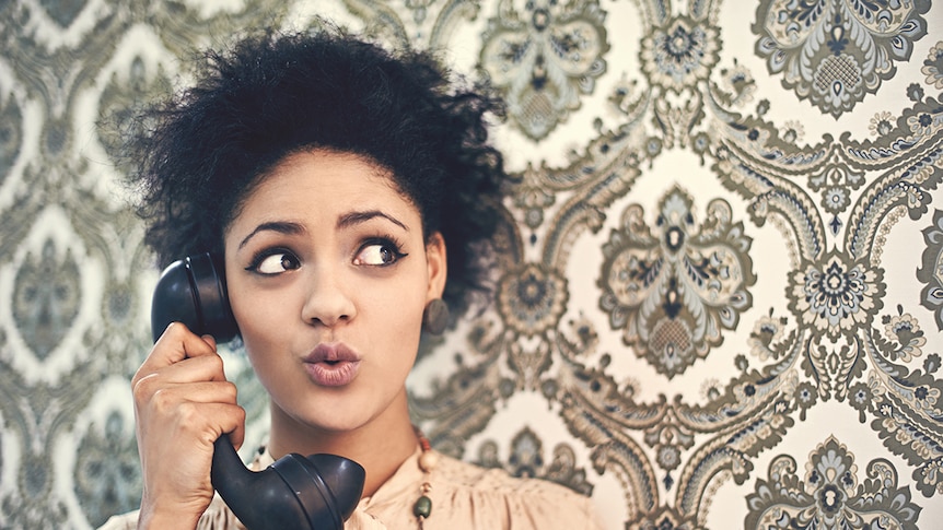 A women in 70s clothing holds an old style landline telephone.