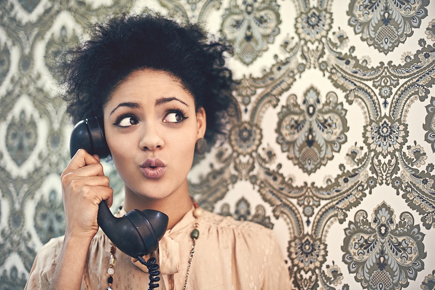 A women in 70s clothing holds an old style landline telephone.