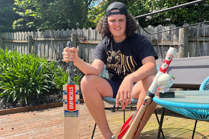 A teenage boy holding a cricket bat in the backyard.