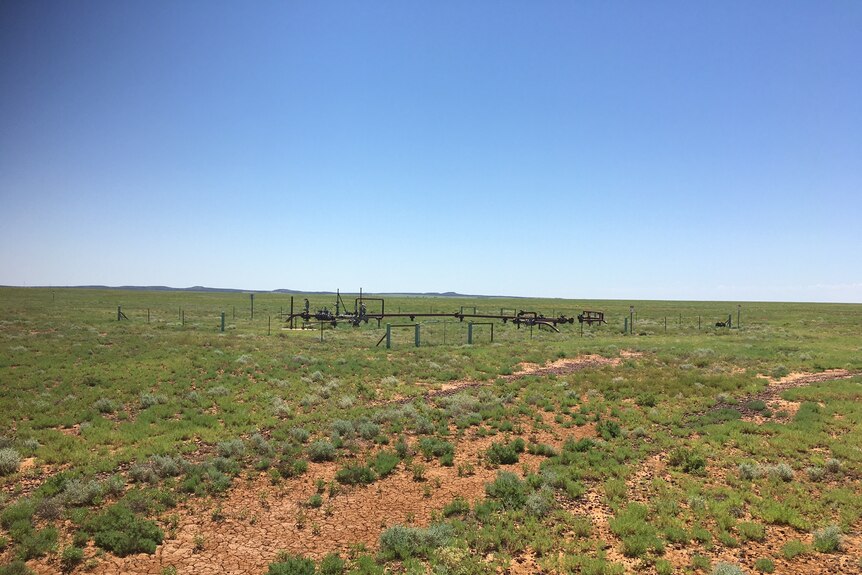 A gas well sits in the distance of a green paddock with fencing surrounding it