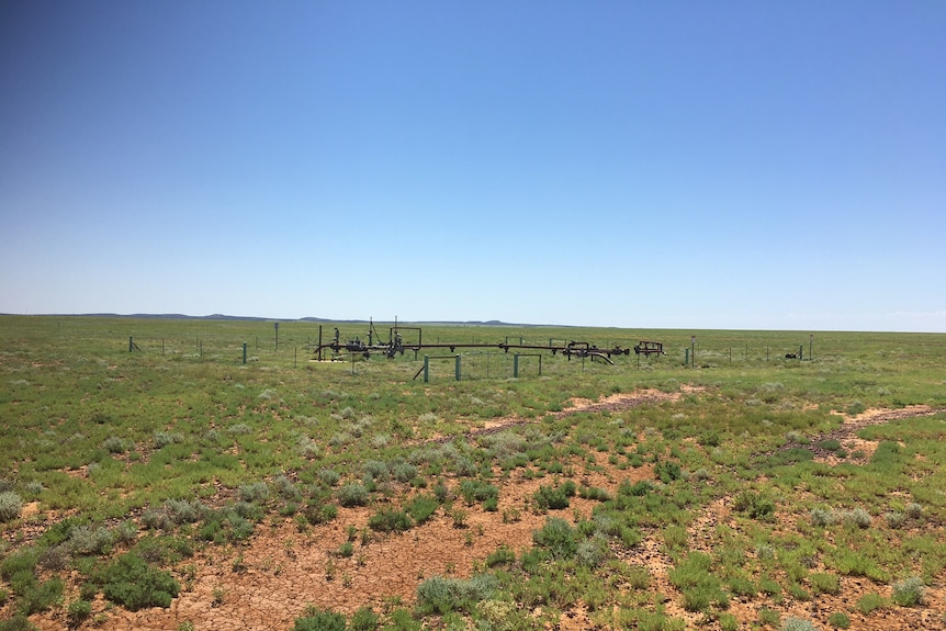 A gas well sits in the distance of a green paddock with fencing surrounding it