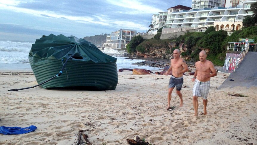 Two men run past a water tank that had been washed up on Bondi Beach