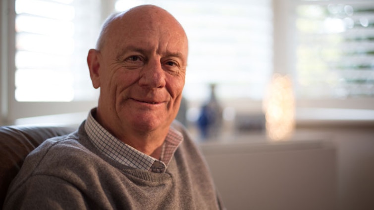 Tim Costello sits in front of set of windows.