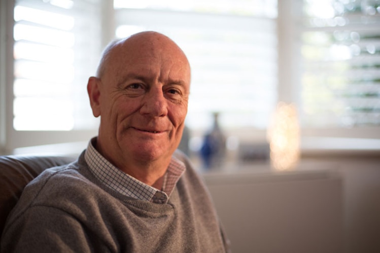 Tim Costello sits in front of set of windows.