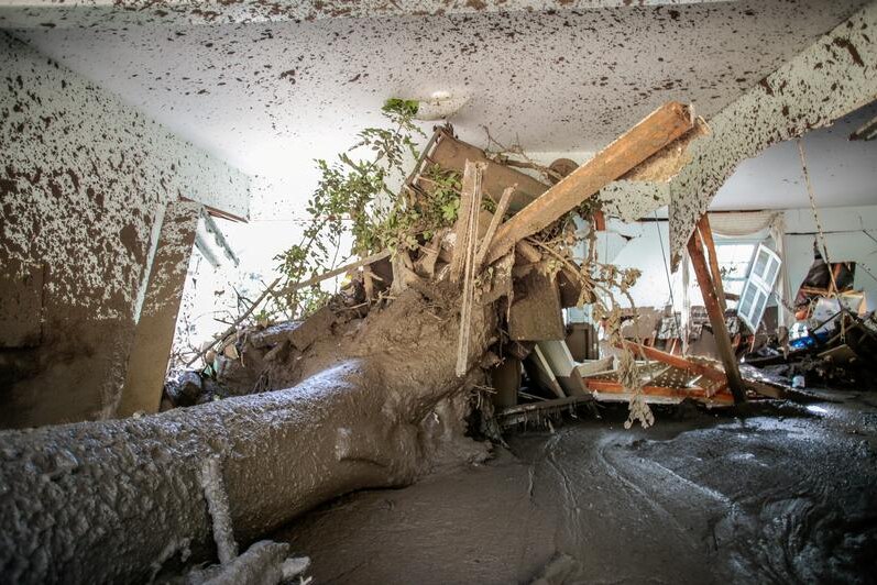 A tree trunk has crashed through a room and mud cakes the walls and floor