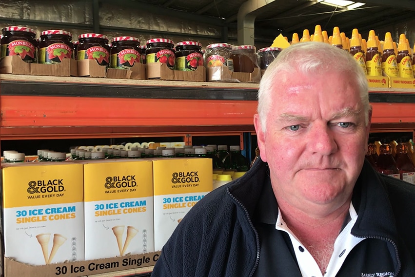 An older, balding man stands in front of supermarket produce.