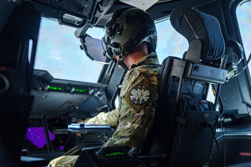 A man in military pilot gear sits in a cockpit 