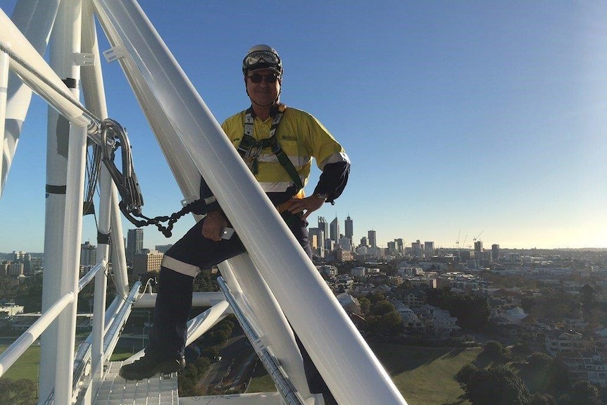 A worker at the top of a steel bridge with the Perth skyline in the background