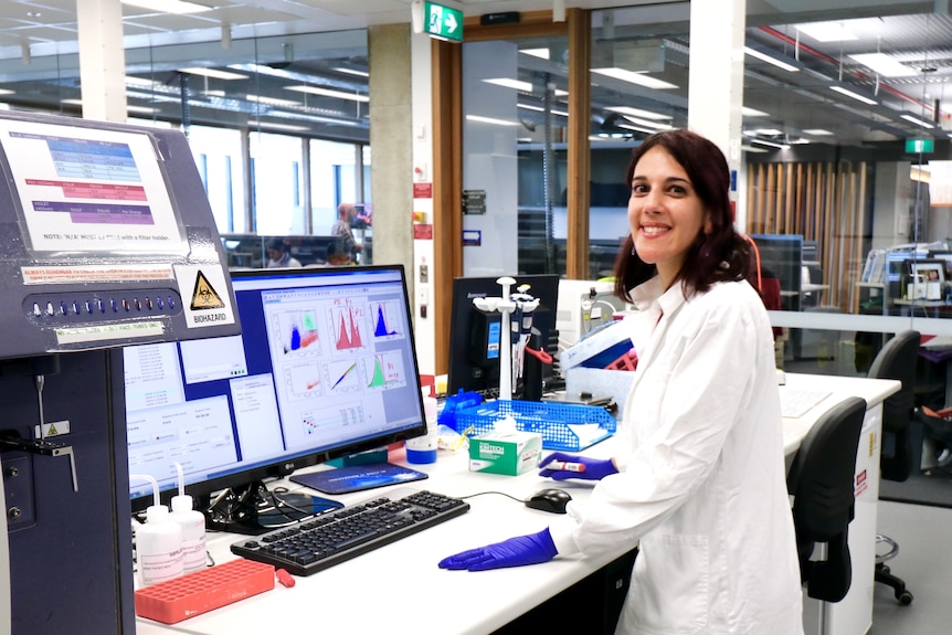 Une femme en blouse de laboratoire sourit en regardant par-dessus son épaule loin d'un ordinateur