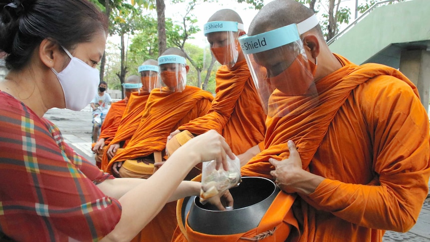 Buddhist monks wear face shields to collect alms during the coronavirus pandemic.