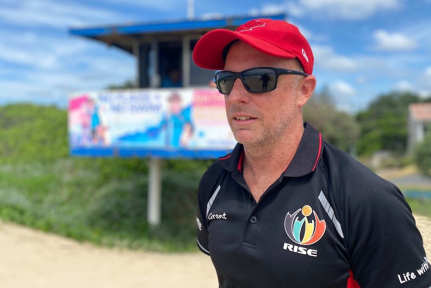 Man stands on a beach looking out to sea, in front of a lifeguard tower