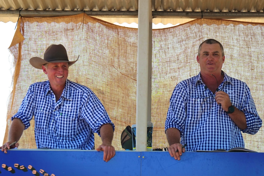 Two men standing next to each other in blue checked shirts, one wearing a cowboy hat