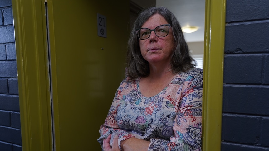 Hotel owner Kate Sinfield stands in the doorway of one of the rooms with a solemn expression